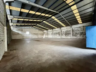 Imagem de um grande espaço industrial com teto de estrutura metálica e paredes de tijolo aparente.