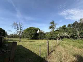 Vista de um campo gramado com cerca e vegetação ao fundo.