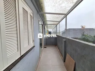 Corredor interno com piso claro e estrutura de vidro que oferece uma vista externa.