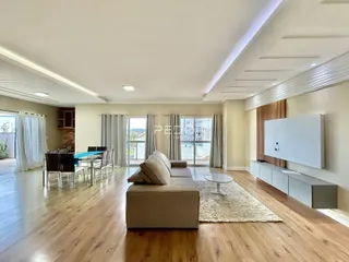 Sala de estar ampla com piso de madeira e grandes janelas.