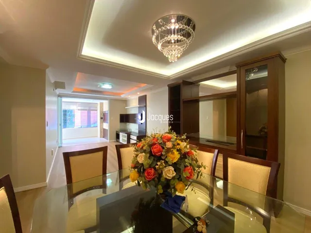 Interior de uma sala de jantar com mesa de vidro e decoração floral.