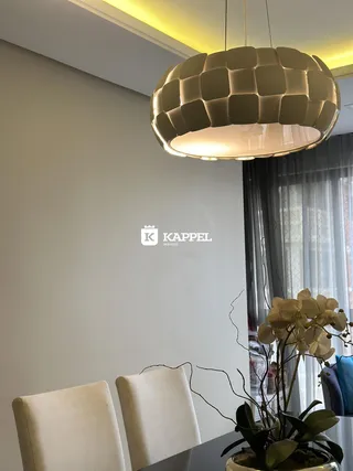 Uma sala de estar com cadeiras claras e uma luminária pendente moderna.