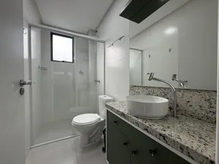 Banheiro moderno com box de vidro, pia de mármore e revestimento de piso claro.