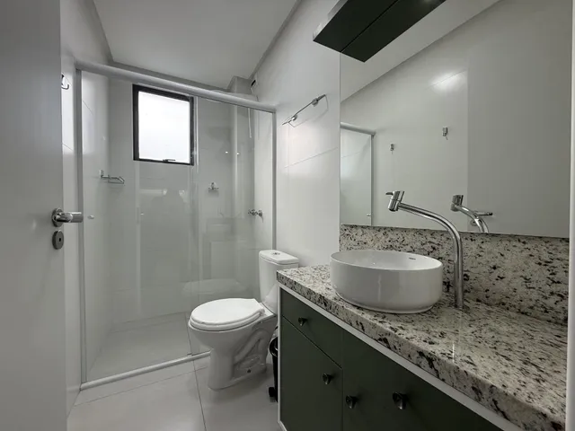 Banheiro moderno com box de vidro, pia de mármore e revestimento de piso claro.