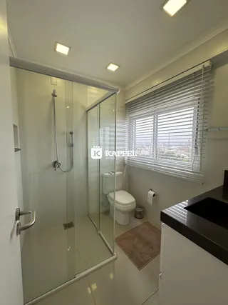 Banheiro com box de vidro e janela mostrando o interior da residência.