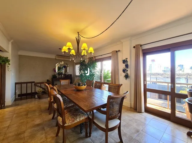 Sala de jantar com mesa de madeira e grandes janelas.