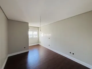 Interior de uma sala com piso de madeira escura e paredes claras.