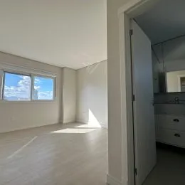 Foto interna de uma sala com piso de madeira clara e janela.