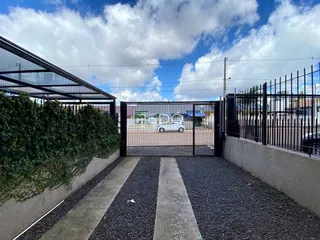 Vista da entrada de uma propriedade com portão e cerca de metal.