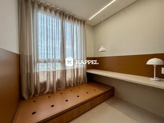 Vista interna de uma sala com cortinas e um banco de madeira ao longo da janela.