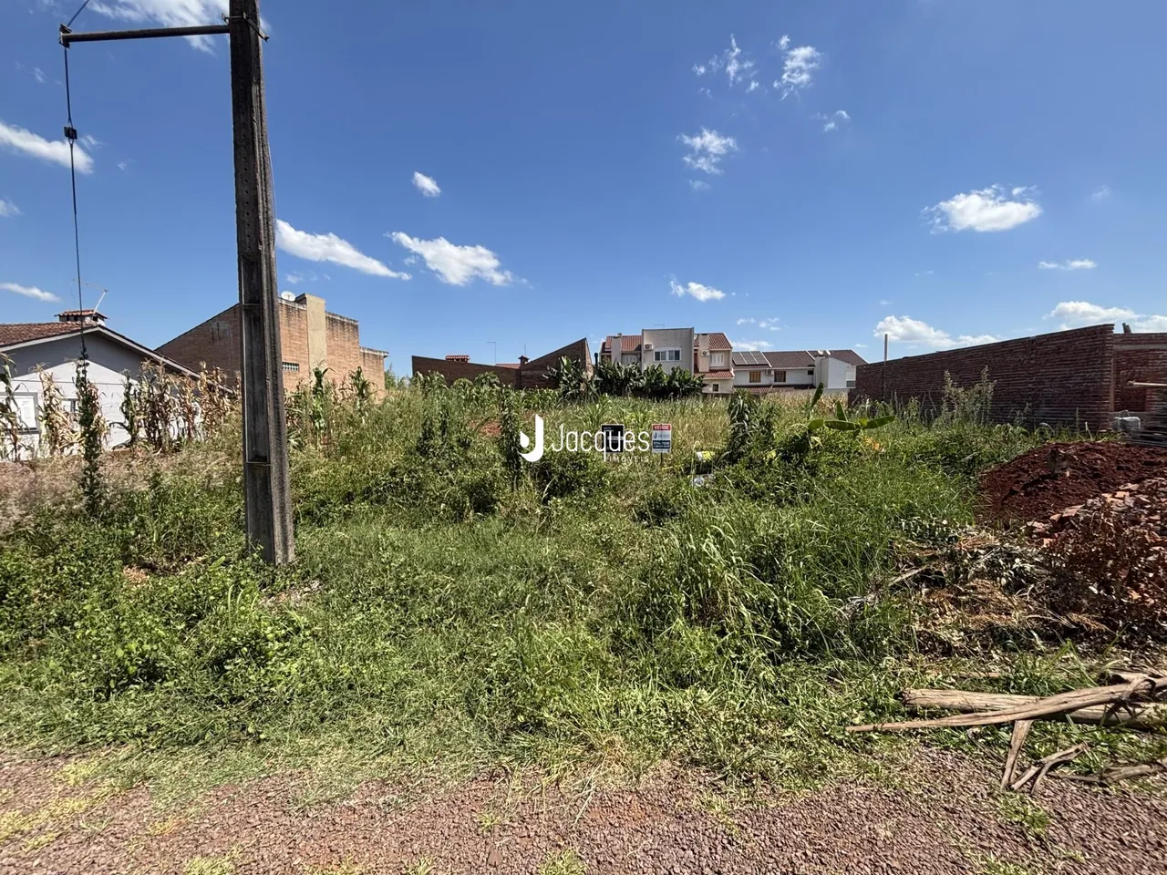 Vista externa de terreno com vegetação densa e estruturas ao fundo.