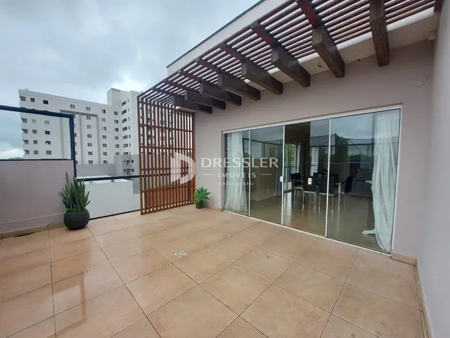 A foto mostra a área externa de uma residência com piso de cerâmica e uma estrutura de madeira.