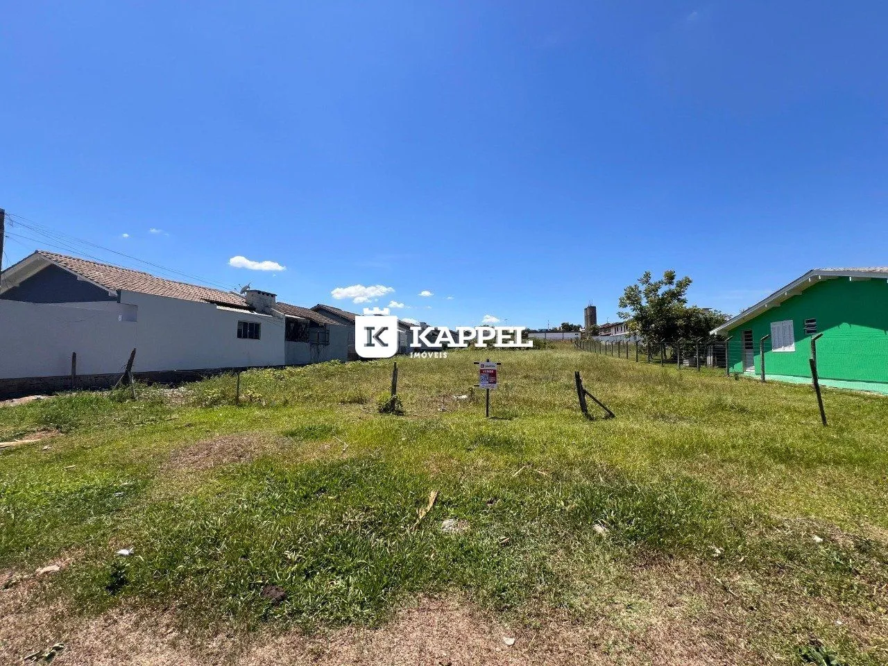 Vista externa de uma propriedade com grama e edifícios ao fundo sob um céu azul.