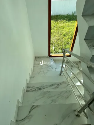 Escadaria interna com degraus de mármore branco e corrimão metálico.