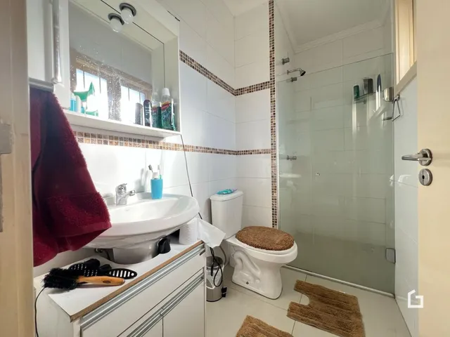 Foto de um banheiro com revestimento cerâmico e box de vidro.
