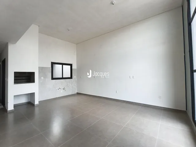 Ambiente interno de uma sala ampla com paredes brancas e piso de cerâmica.