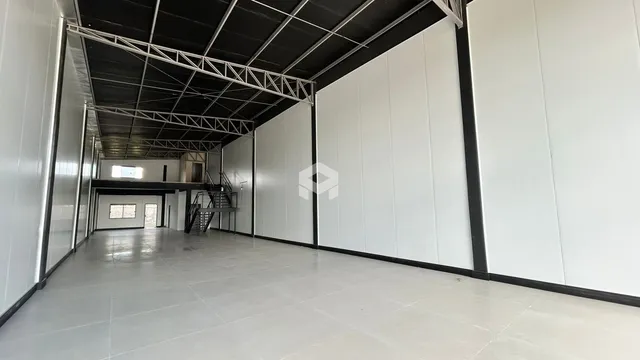 Interior de um grande espaço com teto de estrutura metálica exposta.