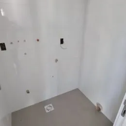 Vista de um corredor interno com paredes brancas e piso claro.