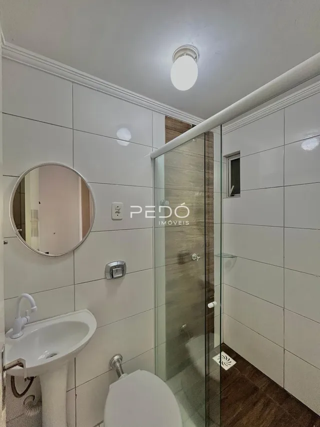 Foto de um banheiro com box de vidro e louças sanitárias brancas.