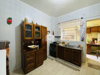 Vista interna de uma cozinha com armários de madeira e azulejos brancos.