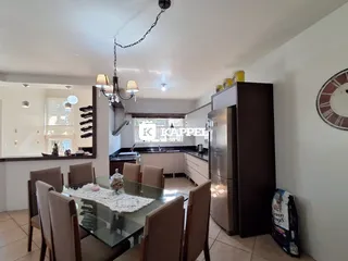 Foto de uma sala de jantar com mesa de vidro e área de cozinha moderna.