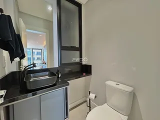 Vista de um banheiro com bancada escura e vaso sanitário branco.