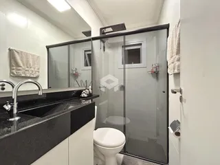 Interior de um banheiro com box de vidro e pia de granito escuro.