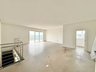 Ambiente amplo com piso claro e acesso a uma varanda com vista da cidade.