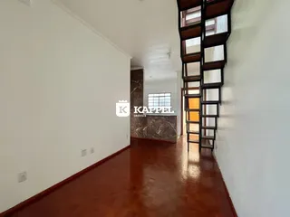 Hall de entrada com piso de madeira polida e escadaria escura.