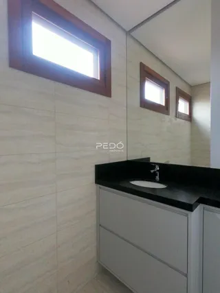 Vista de um banheiro com bancada escura e armários brancos.