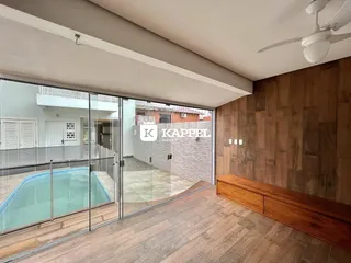 Sala de estar com piso de madeira que se abre para uma área externa com piscina.