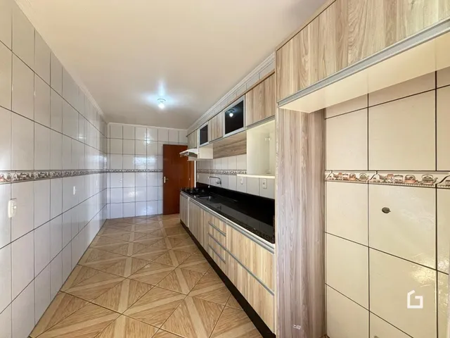 Vista de um corredor com revestimento de cerâmica e armários de madeira na cozinha.