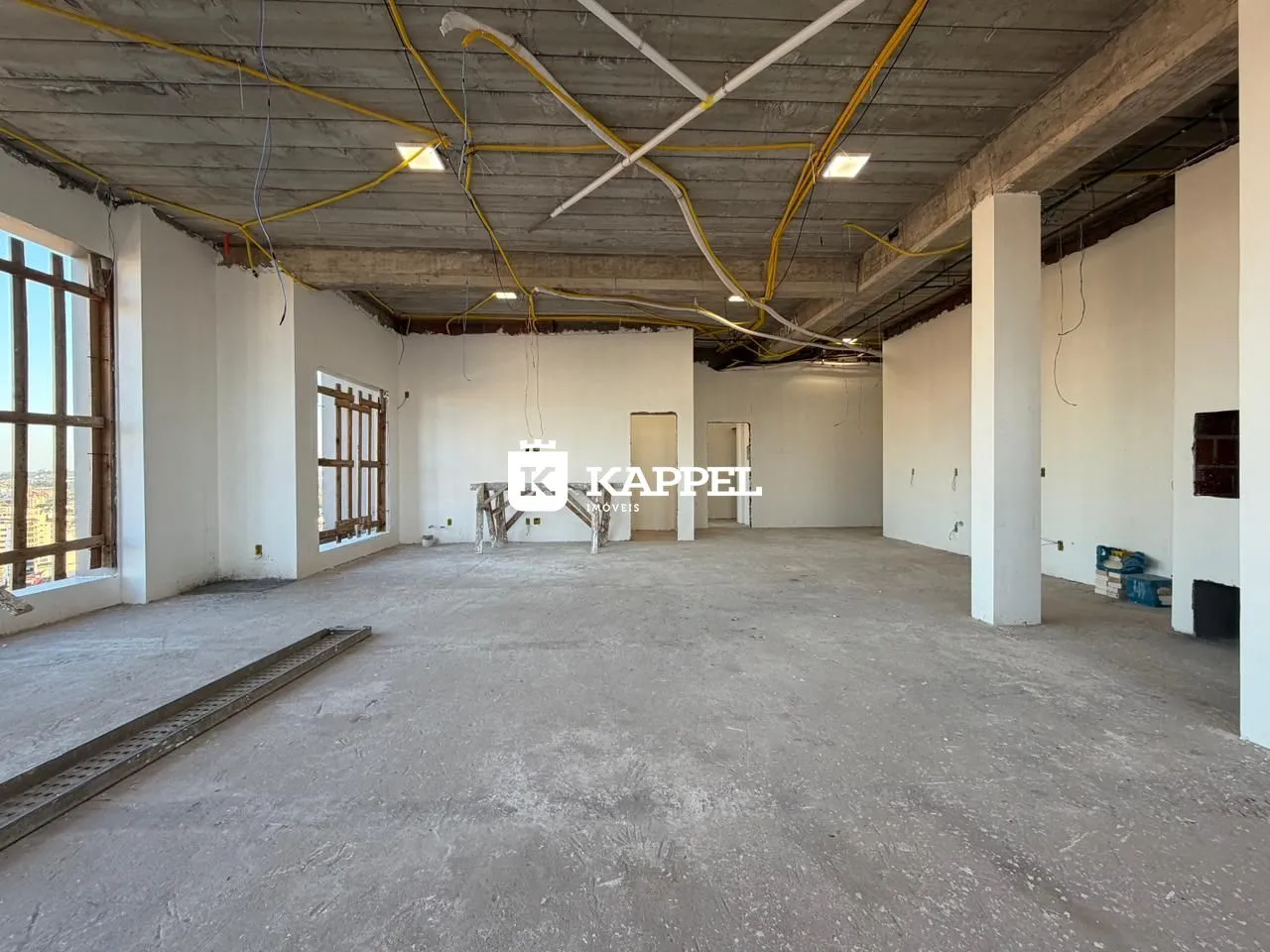 Vista interna de um espaço amplo com estrutura de concreto aparente e tubulações expostas.