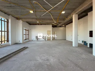Vista interna de um espaço amplo com estrutura de concreto aparente e tubulações expostas.