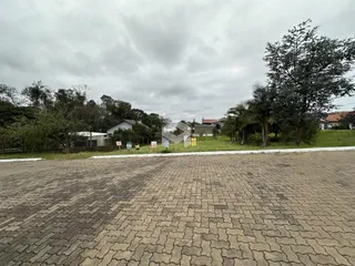Vista externa de uma propriedade com área pavimentada e vegetação ao fundo.