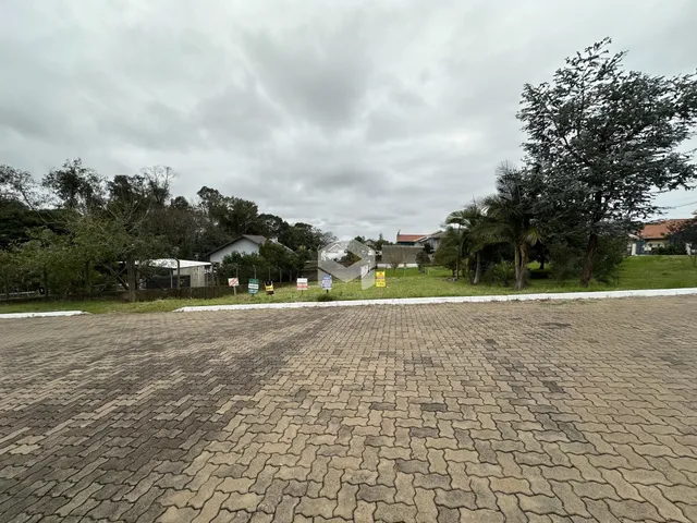 Vista externa de uma propriedade com área pavimentada e vegetação ao fundo.