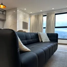 Sala de estar com sofá escuro e cortinas claras.