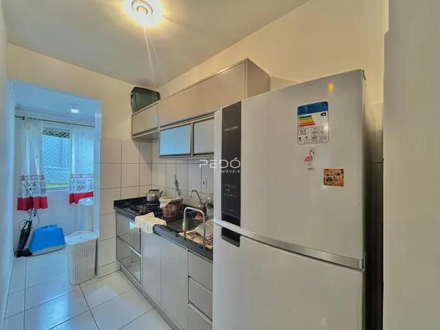 Interior de uma cozinha com armários brancos e piso de cerâmica.