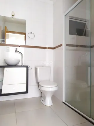 Interior de um banheiro com revestimento cerâmico branco e box de vidro.