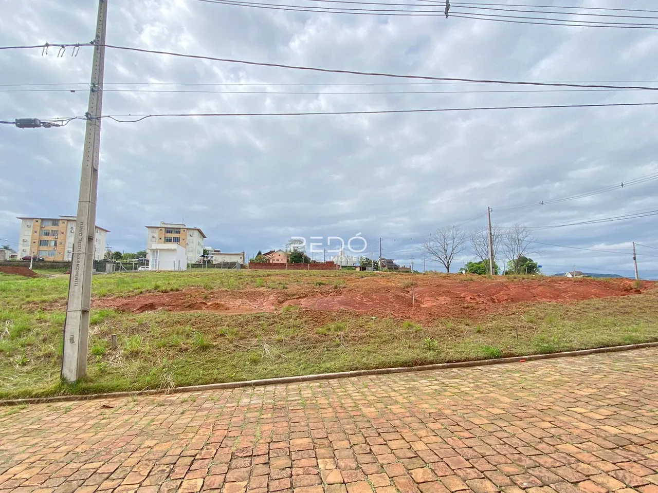 Vista externa de uma propriedade com terreno gramado e edificações ao fundo.