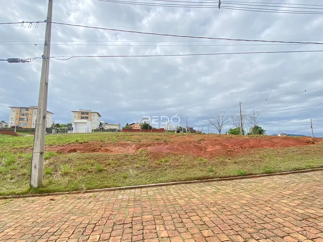 Vista externa de uma propriedade com terreno gramado e edificações ao fundo.