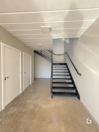 Corredor interno de uma residência com paredes brancas e piso de concreto.