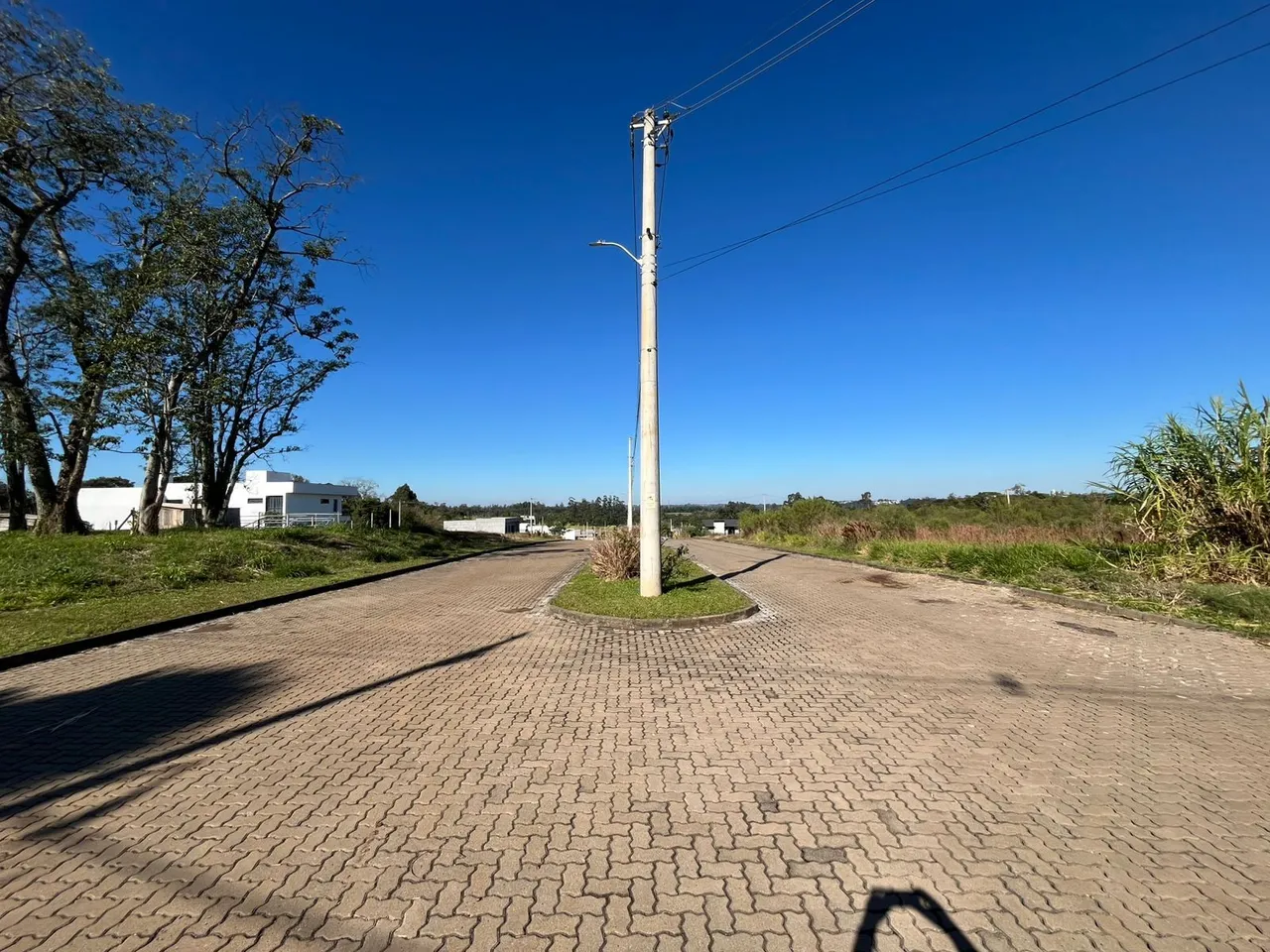 Vista externa de uma rua pavimentada com vegetação ao fundo sob um céu azul.