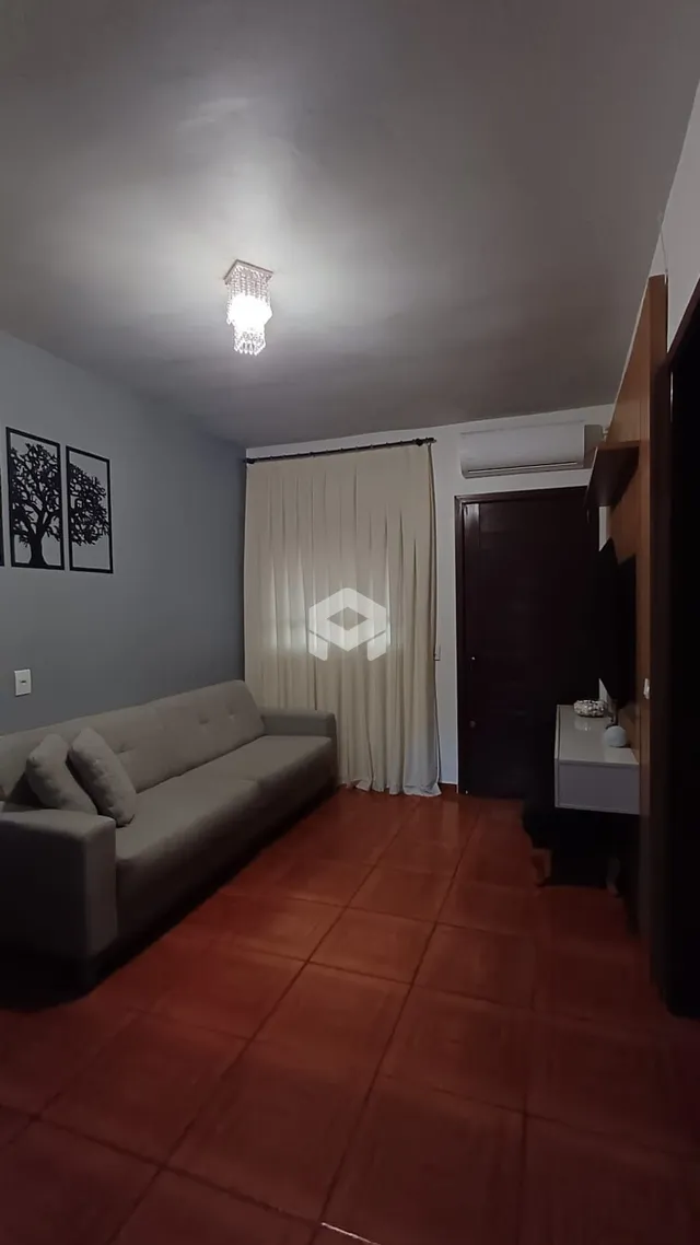 A sala de estar apresenta um sofá cinza e piso de cerâmica avermelhada.
