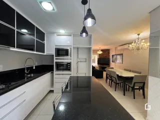 Interior de uma cozinha e sala de jantar moderna com armários brancos e bancadas escuras.