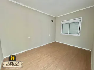 Vista interna de uma sala com piso de madeira clara e paredes bege.