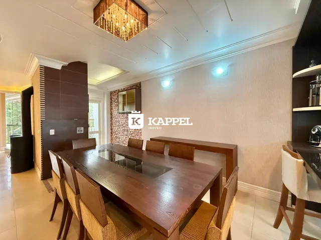Sala de jantar com mesa de madeira escura e cadeiras em um ambiente claro.