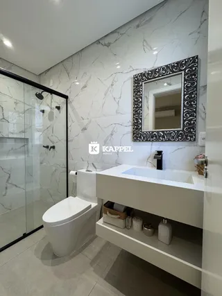 Banheiro moderno com revestimento de mármore branco e box de vidro.