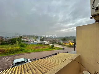 Vista externa de uma residência com vegetação e uma rua no fundo.
