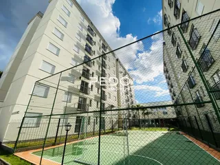 Vista externa de um prédio residencial com cerca de tela e quadra ao fundo.